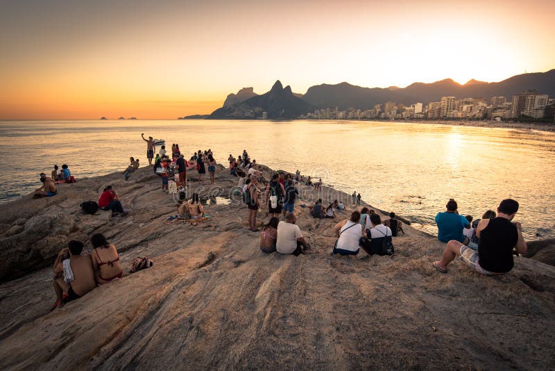 Crowd gathered on Arpoador Rock at sunset watching the sun dip behind Two Brothers Mountain