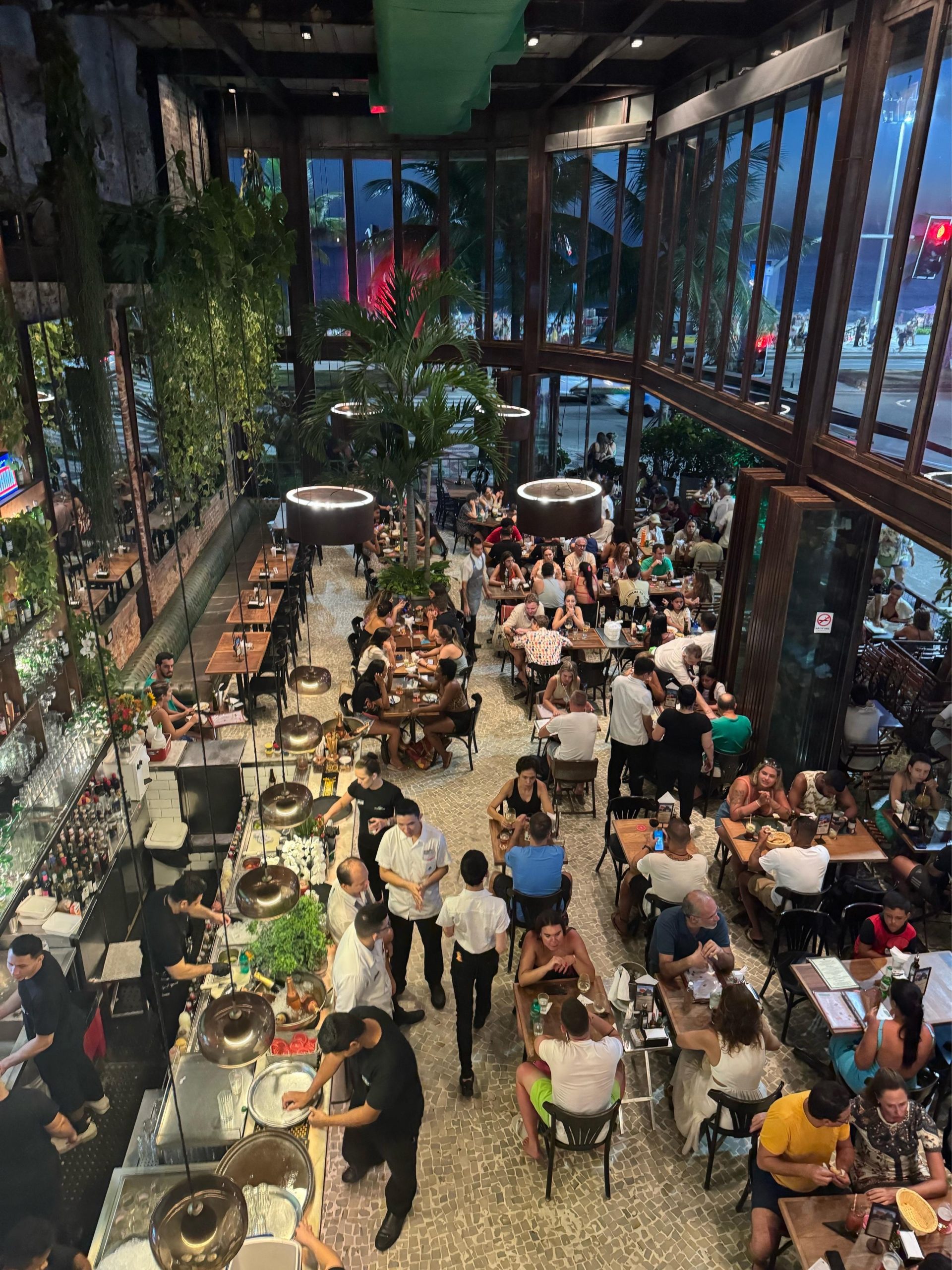 Boteco Belmonte — lively restaurant interior with guests enjoying dinner, tropical plants, and warm ambient lighting